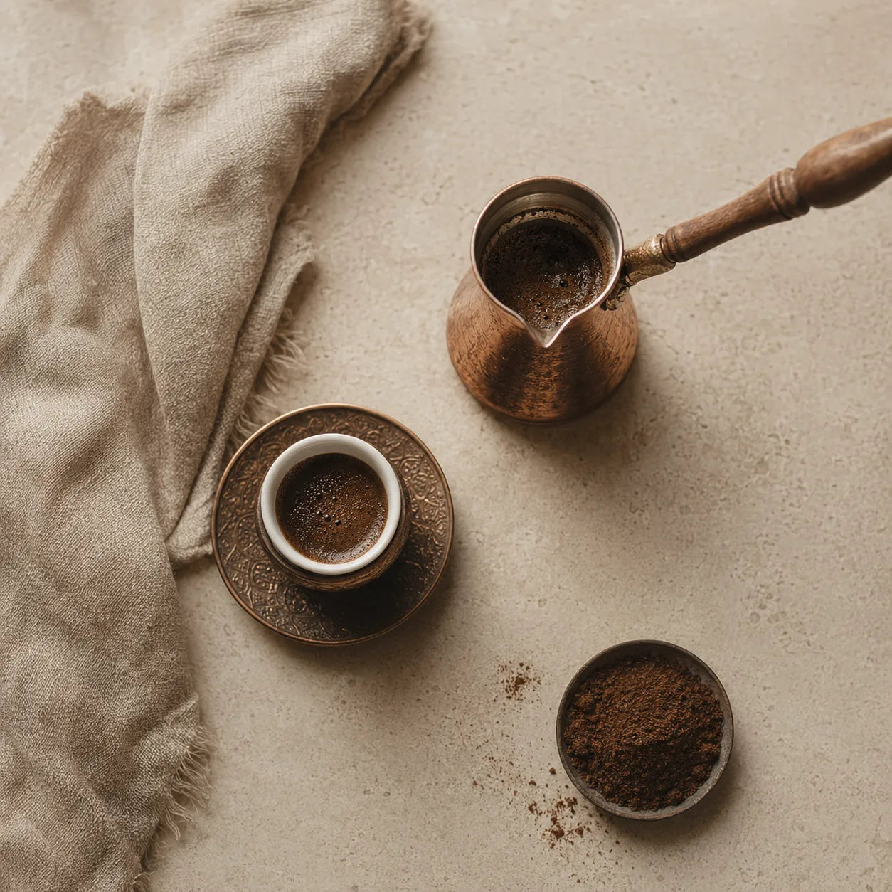 A top-down Turkish coffee brewing setup with a copper cezve and ground coffee.