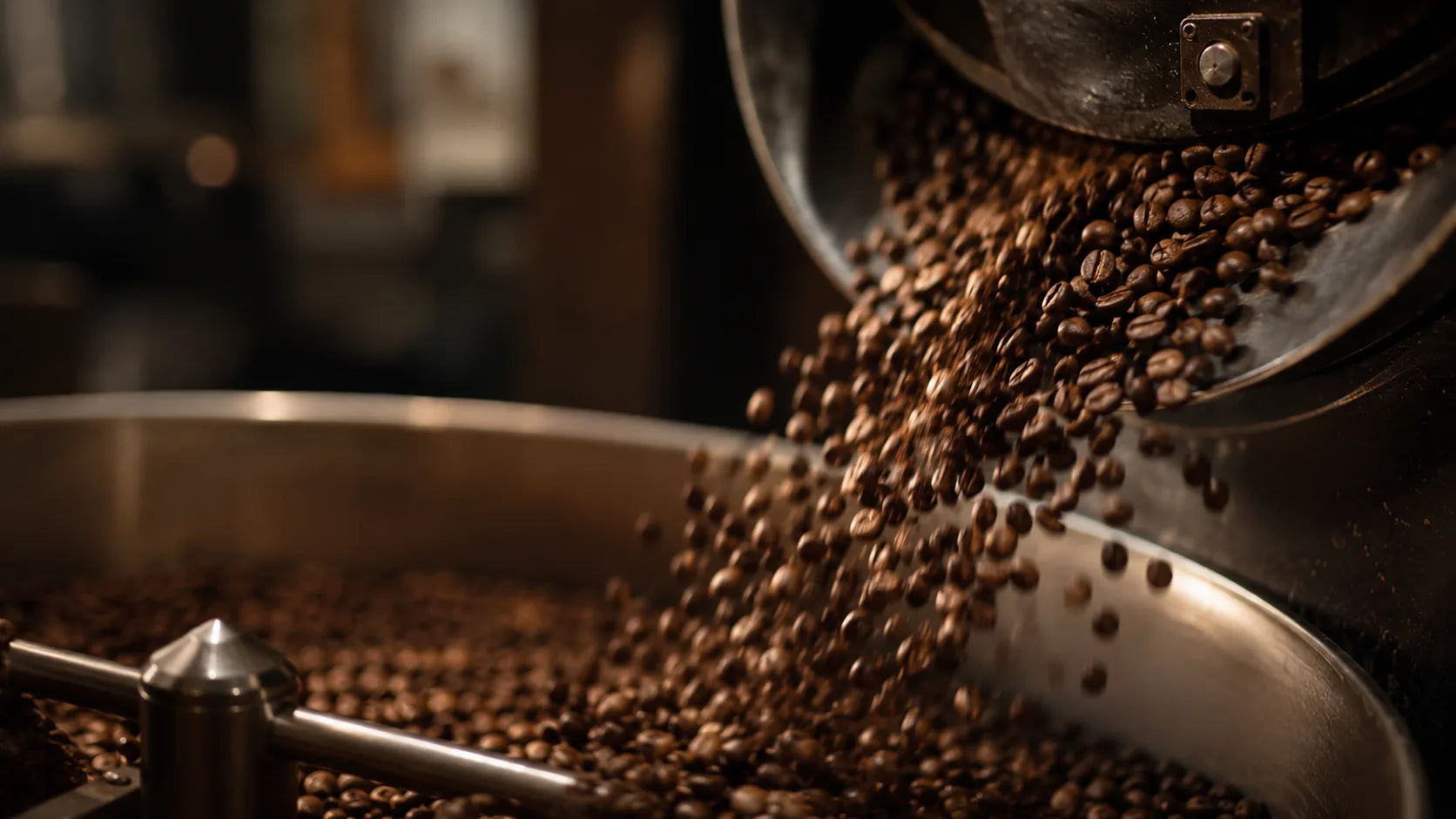 Fresh-roasted coffee beans cascading from a roaster cooling tray in warm light.